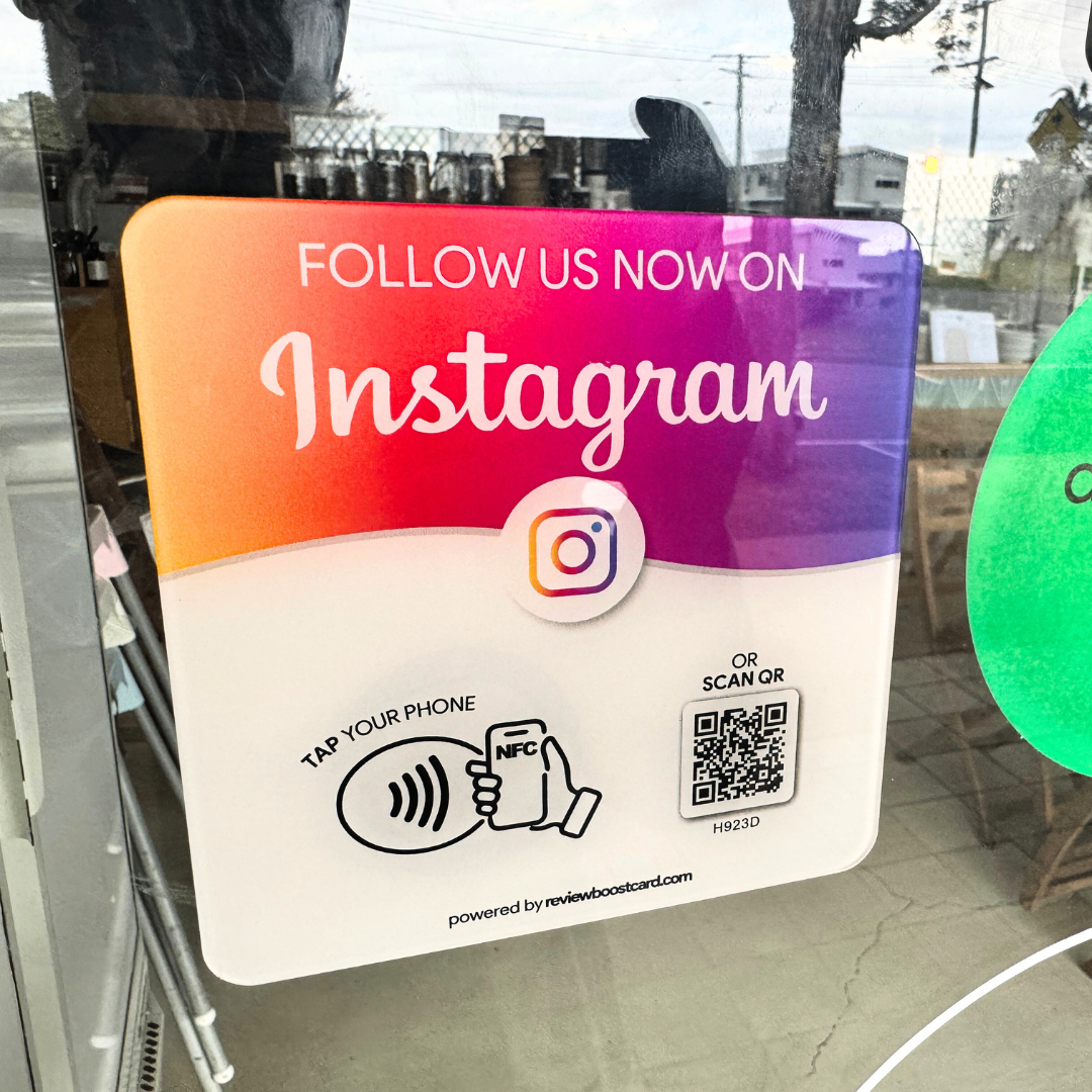 uare plaque with a gradient from orange to purple, featuring the Instagram logo and text "Follow Us Now on Instagram." It offers options to "Tap Your Phone" using NFC or "Scan QR" code, powered by reviewboostcard.com, displayed on a window